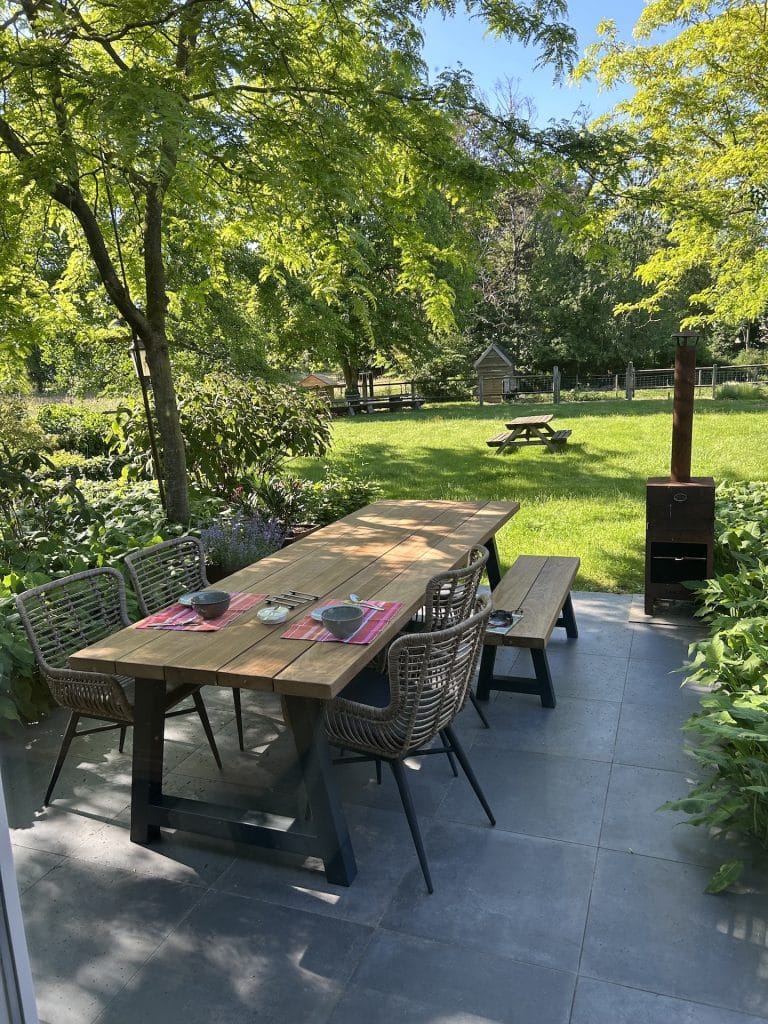 Irokohouten tuintafel Tjerk geplaatst op terras in een tuin.
